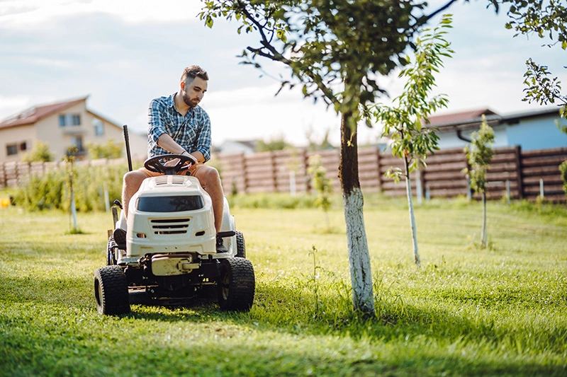 Mann auf Aufsitzrasenmäher beim Rasenmäher im Zuge von Hausmeistertätigkeiten